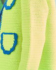 Close-up of a crocheted lime green sweater with blue scalloped trim on the pocket and edges, highlighting detailed stitching similar to the Russell Cardigan by Hunter Bell NYC.