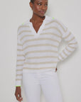 Against a light background, a person wears the Lisa Todd "Stripescape," a white and beige V-neck cotton sweater with neon green accents, teamed with white pants. The textured knit adds depth to their look, while their short hair and relaxed expression complete the image.