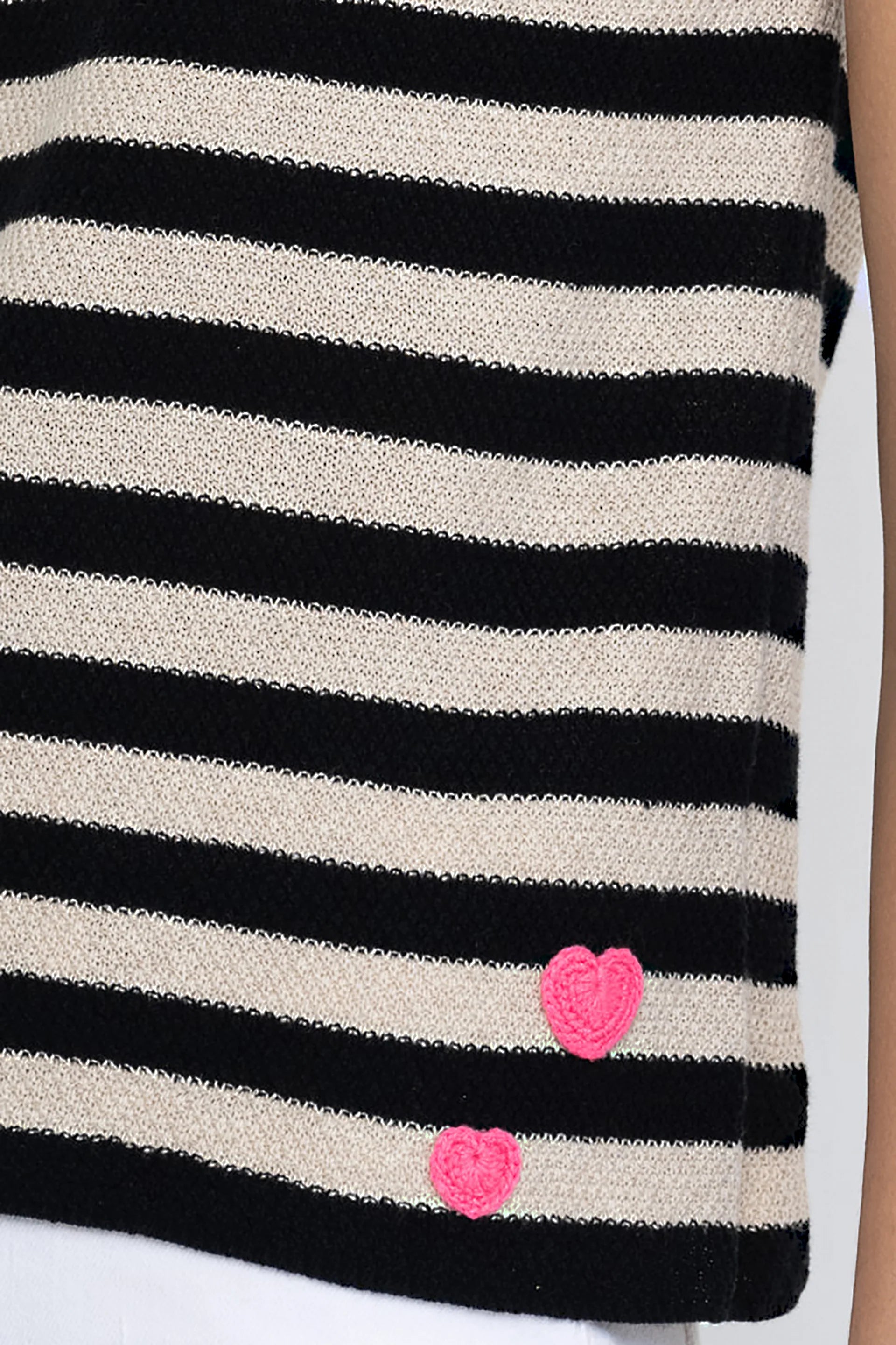 The Lisa Todd Summer Lovin Sweater is a black and beige striped sleeveless crew neck tank, featuring two small pink crochet hearts near the bottom hem. Only part of the model's arm and torso are visible.