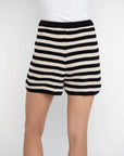 A person is shown from waist to mid-thigh against a plain light background, wearing the Lisa Todd Summer Lovin Short in black and white stripes with an elastic waist, paired with a white top.