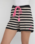 A person wears the Lisa Todd Summer Lovin Short in black and white stripes with an elastic waist, pink drawstring, and two pink dots near the hem, paired with a white top.