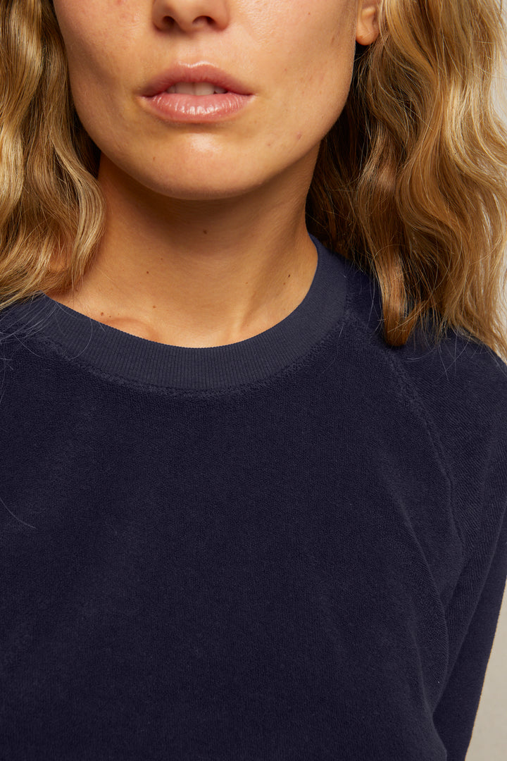 A close-up of a woman with wavy blonde hair wearing the Perfectwhitetee Saylor Loop Terry Sweatshirt, showing her lips, chin, neck, and shoulders.