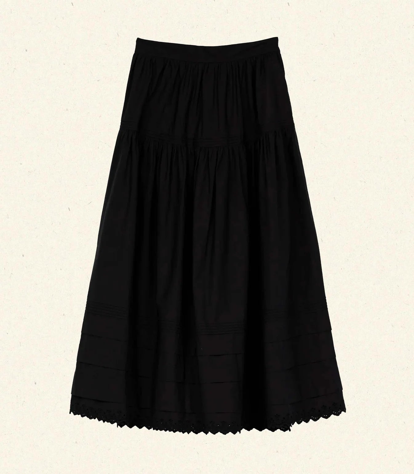 The Sebastiane Skirt by DOEN is a black, high-waisted A-line skirt in organic cotton with gathered fabric and subtle lace trim at the hem, shown against a light beige background.