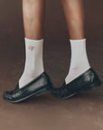 Black loafers styled with The Great Inc. Monogrammed Trouser Sock, shown standing on a brown surface.