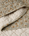 A close-up of the Blossom Hand Stitched Quilt by Coyuchi Inc shows its beige, blue, and brown floral design, with a cream diamond-stitched underside—crafted from organic cotton for comfort and style.