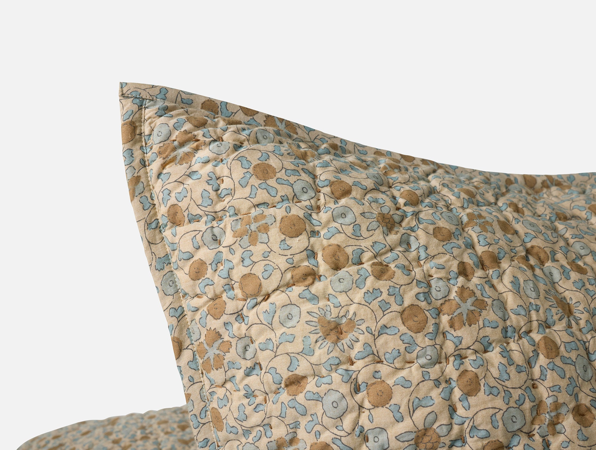 Close-up of the Blossom Hand Stitched Euro Sham by Coyuchi Inc, featuring a blue and brown vintage Sarasa print on soft, textured organic cotton with handstitched detailing and a beige background.