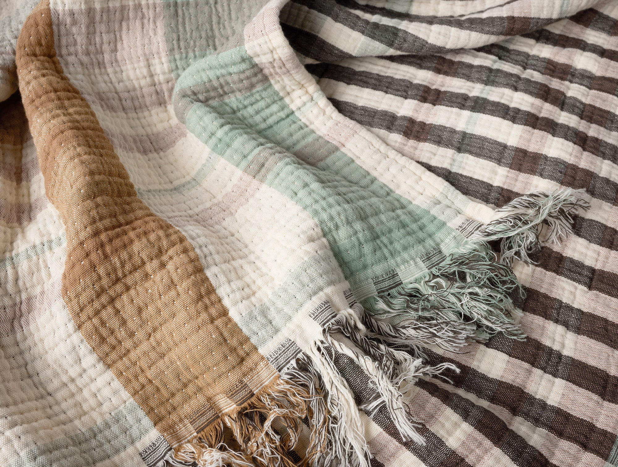 The Coyuchi Inc Loma Matelasse OS Throw features textured stripes in brown, cream, mint green, and gray on organic cotton. Soft with a slightly crumpled look, it’s finished with fringed tassels at the edges.