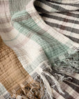 The Coyuchi Inc Loma Matelasse OS Throw features textured stripes in brown, cream, mint green, and gray on organic cotton. Soft with a slightly crumpled look, it’s finished with fringed tassels at the edges.