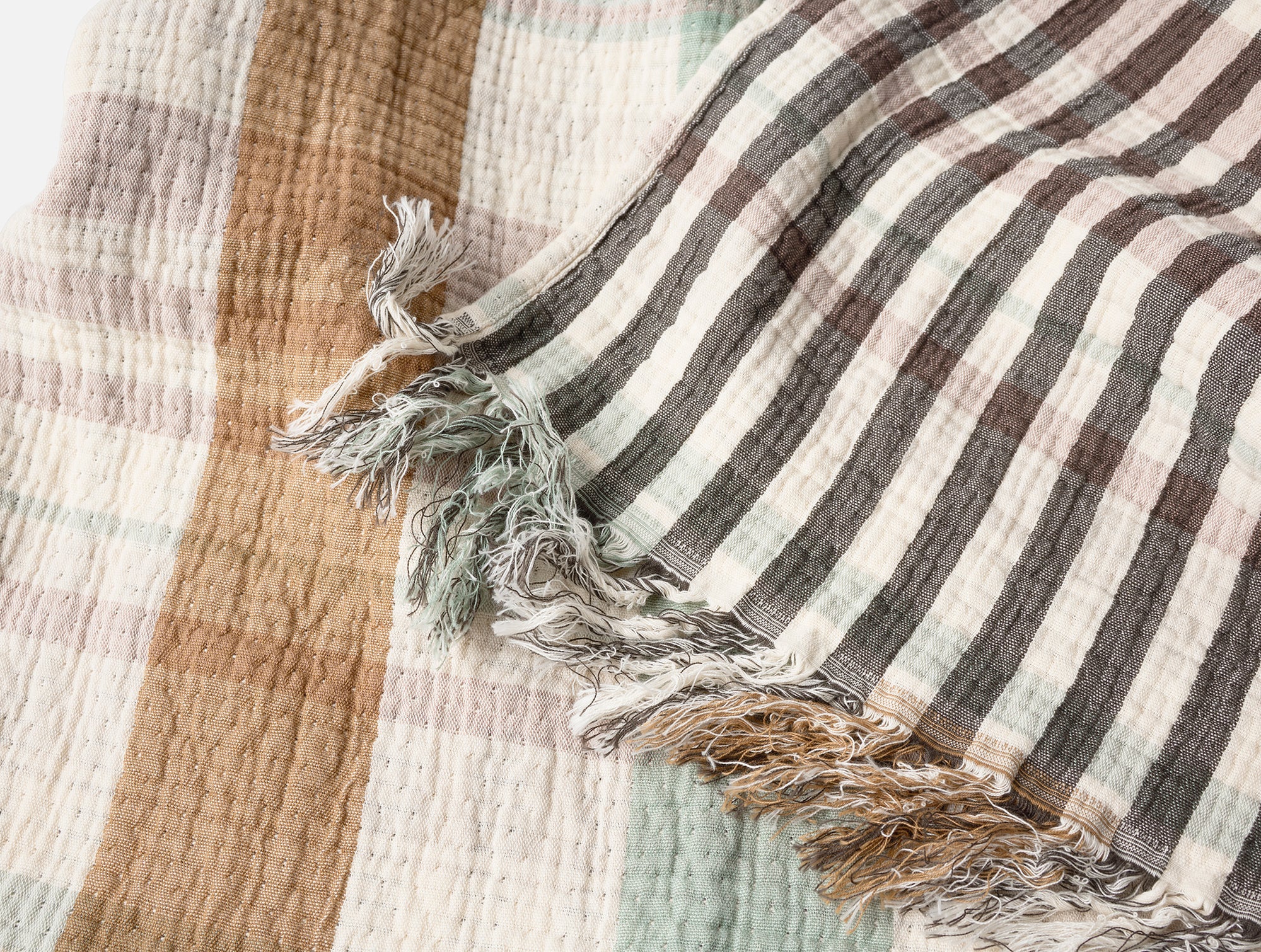 The Loma Matelasse OS Throw by Coyuchi Inc features beige, brown, gray, and light green stripes with a crinkled texture and frayed edges. Made from organic cotton, this eco-friendly throw adds a soft, rustic touch to any space.
