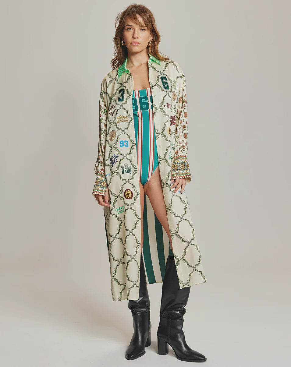 A woman stands against a plain background wearing the Me369 Athena Collar Button Up over a green and white striped swimsuit, styled with hoop earrings and black knee-high boots.