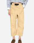 The lower half of a person is shown wearing Sea New York’s Andrea WorkWear Pants—wide-leg, cropped, tan trousers with large front pockets—styled with a black belt, brown shoes, and a light blue shirt with white cuffs.