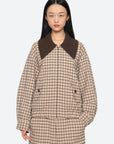 A person with long black hair models the Sea New York Savannah Plaid Jacket, which features an oversized ribbed-knit collar and a contemporary fit, standing against a plain light background.