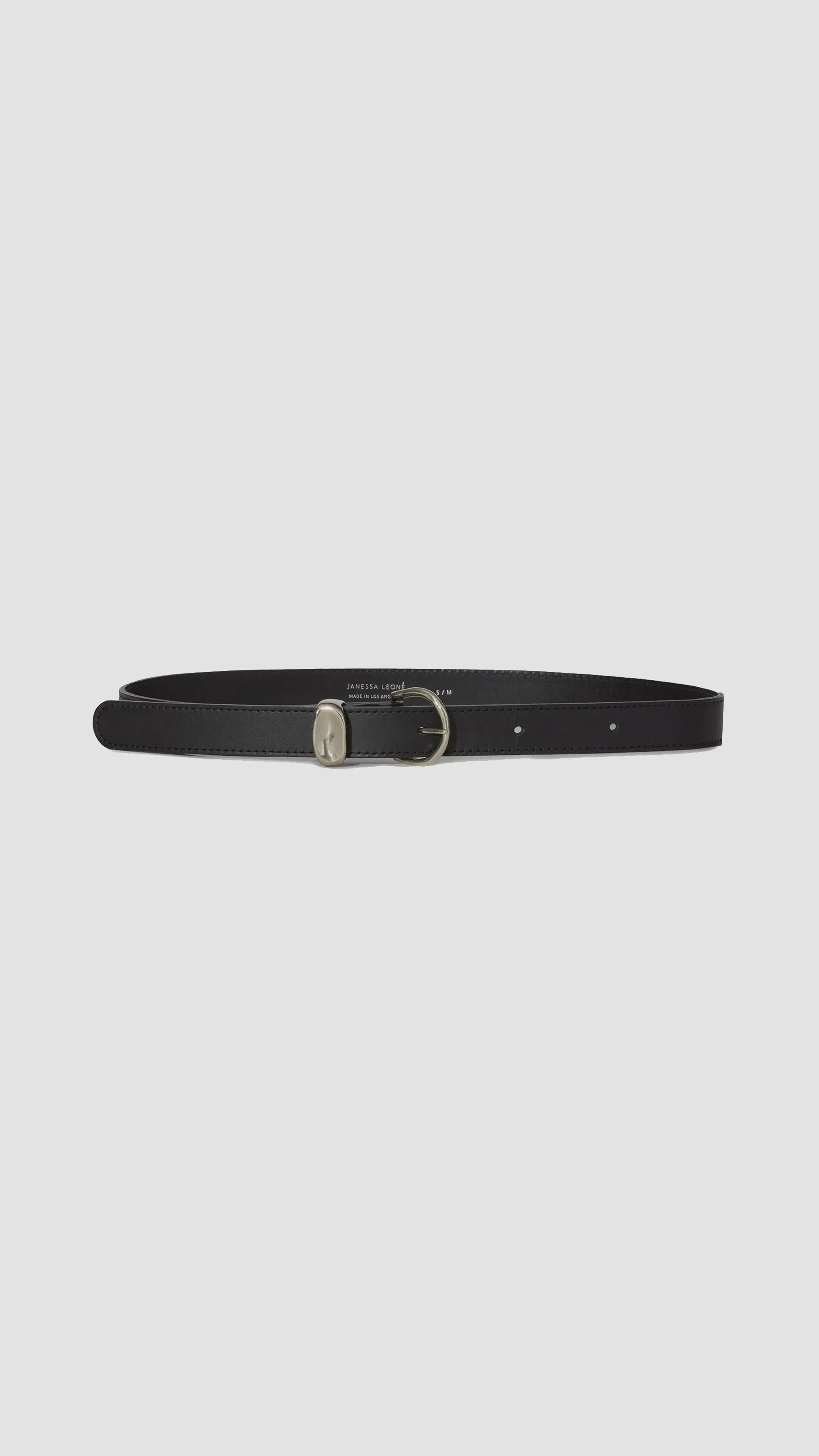 The Janessa Leone Myra is an artisan-crafted thin black leather belt with a small silver buckle, shown lying flat on a plain light gray background—a timeless accessory for any wardrobe.