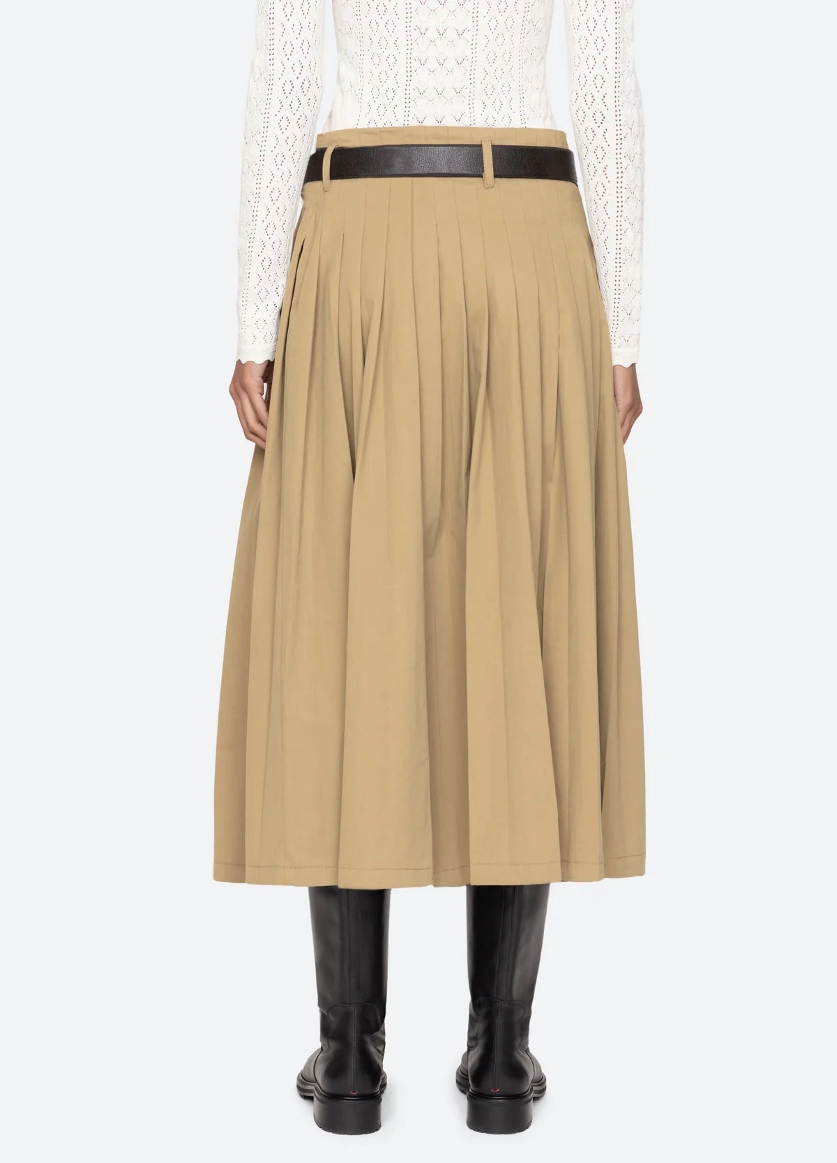 A person shown from the back wears the Sea New York Andrea Workwear Skirt in beige, paired with a black leather belt, a white long-sleeve lace top, and black knee-high boots against a plain background.