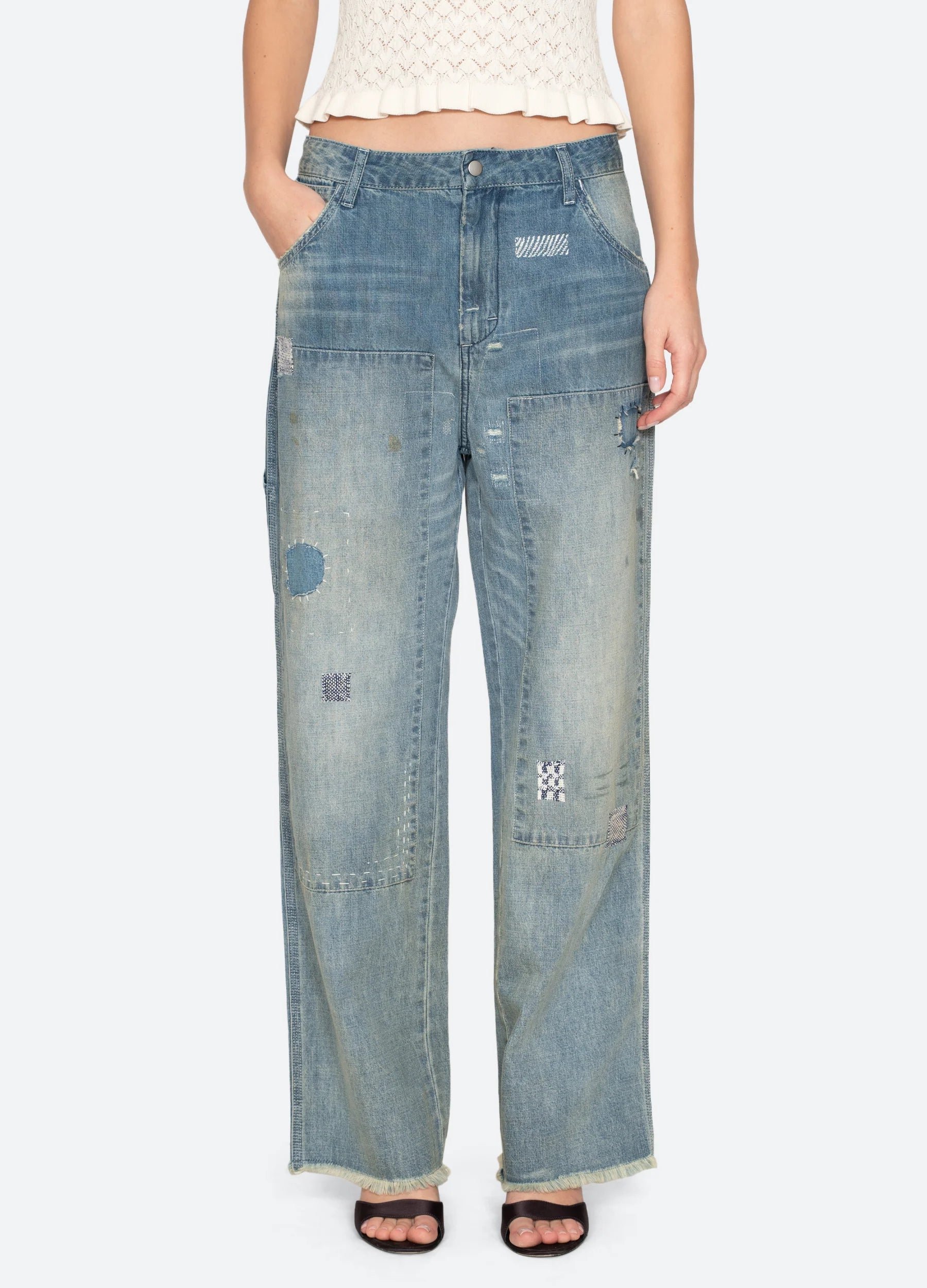 Wearing Sea New York’s Claira Mended Jeans—relaxed fit, wide-leg, high-waist, light-wash patchwork denim with visible stitching—and a sleeveless cream knit top; only the lower torso and legs are visible.