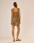 A woman with straight brown hair stands against a plain light background, wearing the sleeveless, artisan-made Jasmine Top by natalie martin in a flowy leopard print paired with black sandals.