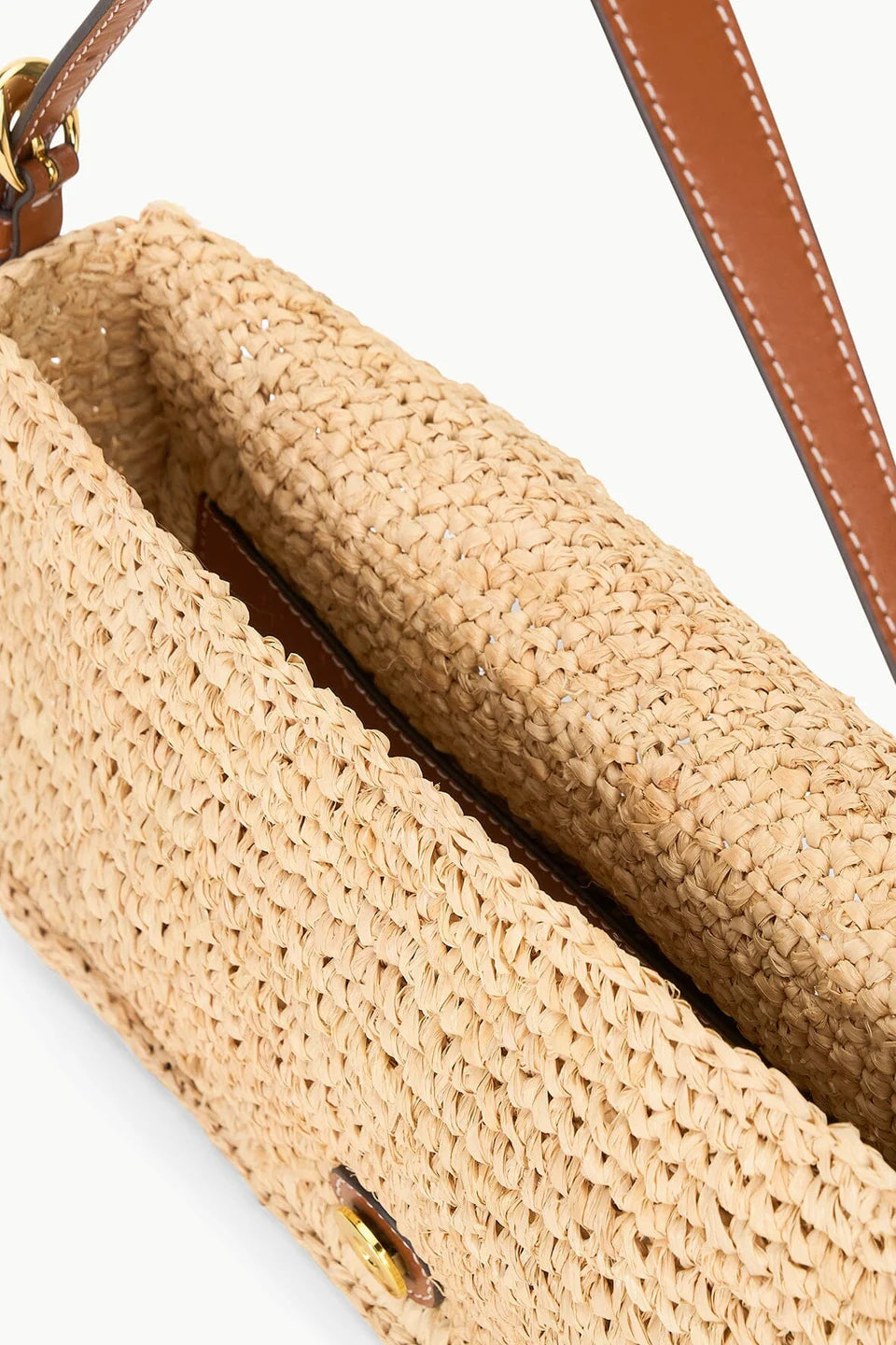 Close-up of the Staud Harlow Raffia Bag in natural, featuring an open top, brown leather-trimmed strap, and a glimpse of the interior lining.