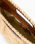 A close-up of the Staud Lena Raffia Clutch shows its woven straw design, tan leather trim and handles, open top with built-in handles, and snap button closure.