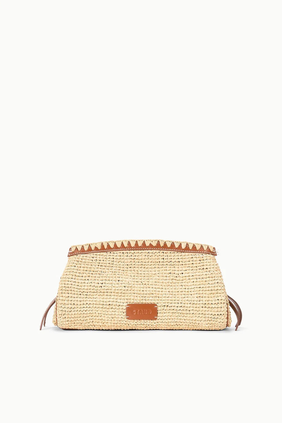 The Maude Convertible Clutch by Staud features woven straw raffia with brown leather trim and a small front leather patch, shown against a plain white background.