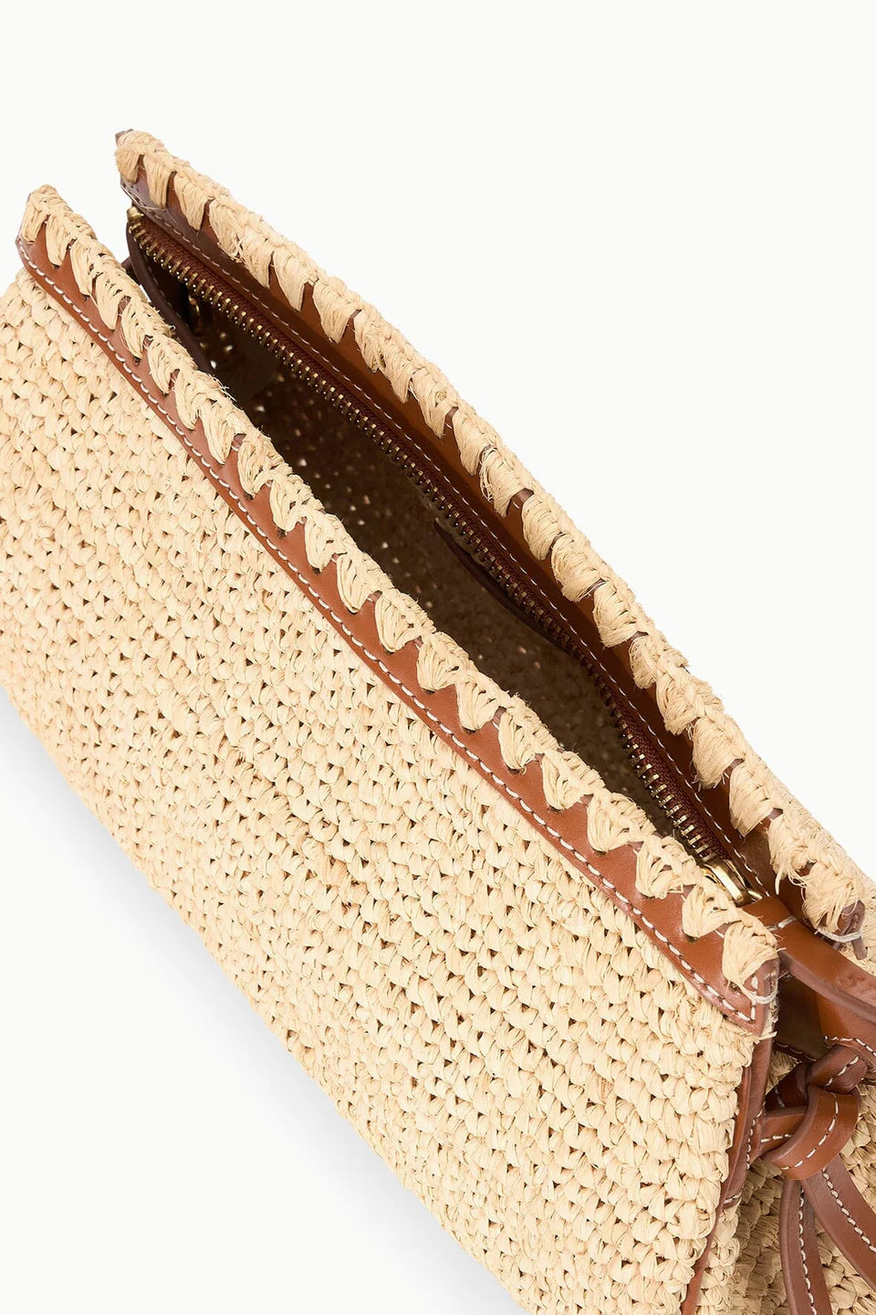 A close-up of the Staud Maude Convertible Clutch /Natural shows its raffia body, brown leather trim, inner zipper, and a leather strap for versatile clutch or shoulder wear.