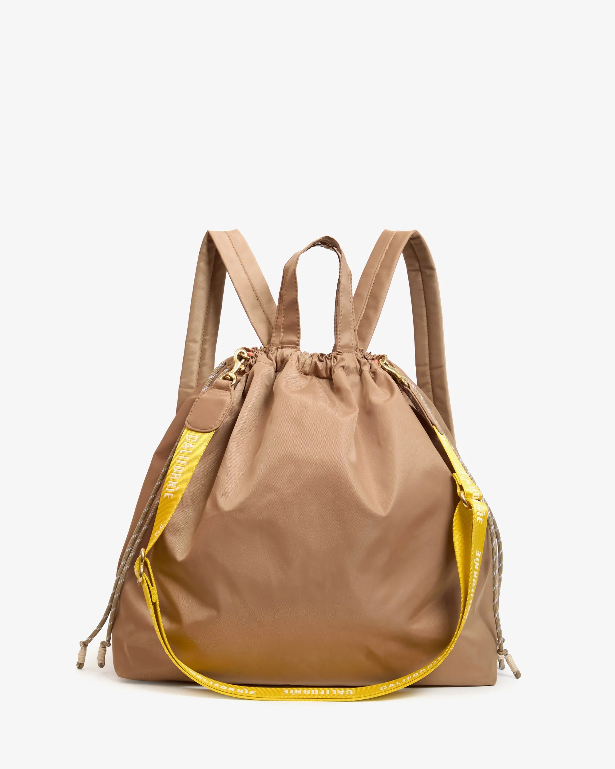 The Clare Vivier Sac Tout Backpack is a tan recycled nylon bag with dual top handles, a yellow adjustable shoulder strap, gold hardware, and a small yellow tag.