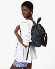 A woman wears a white long-sleeve shirt with blue stripes and matching shorts, posing confidently with the Clare Vivier Sac Tout Backpack over her shoulder against a plain white background.