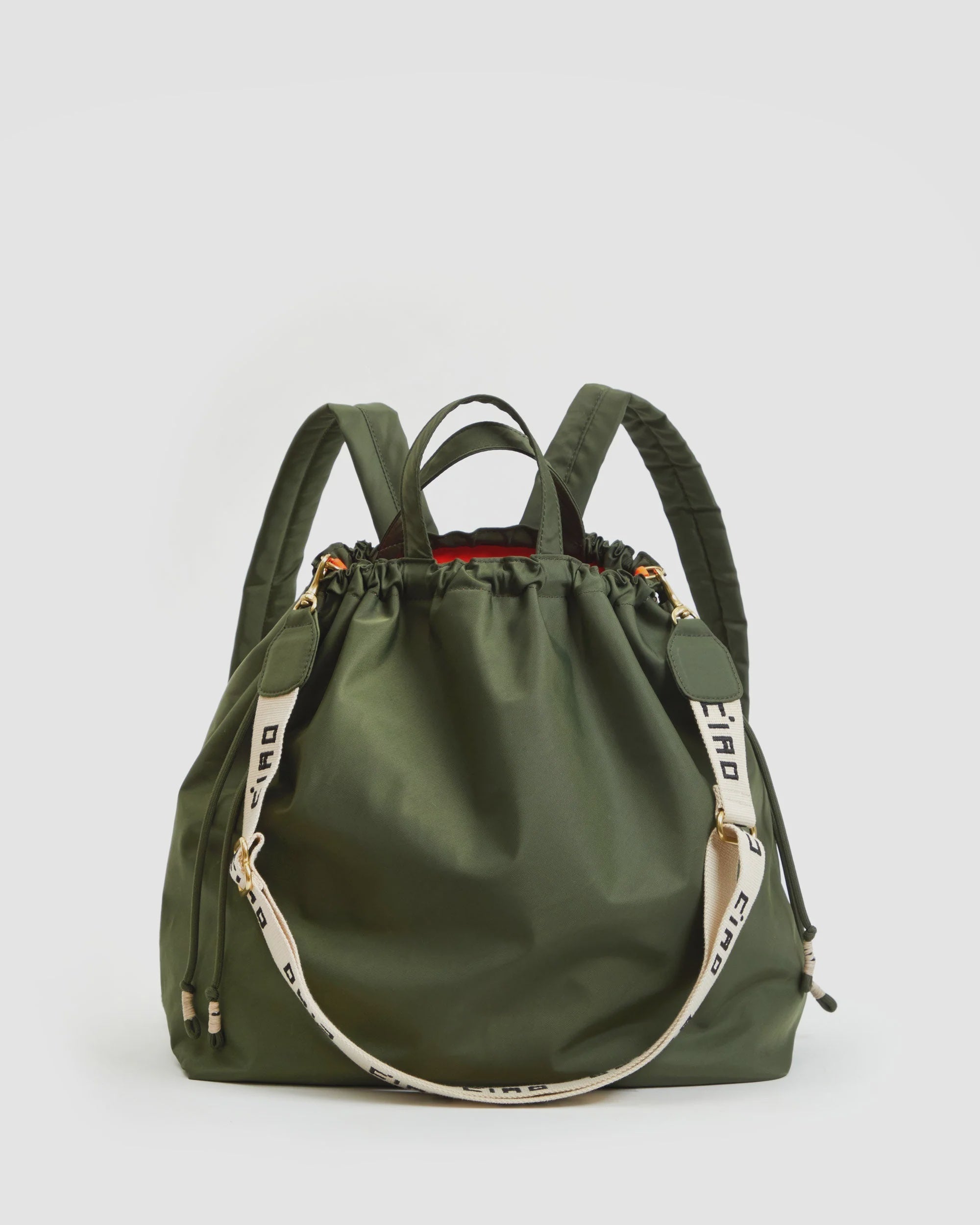 The Clare Vivier Sac Tout Backpack is a large olive green recycled nylon bag with two top handles, adjustable shoulder straps, a detachable cream strap with black text, drawstring closure, and gold-tone hardware.