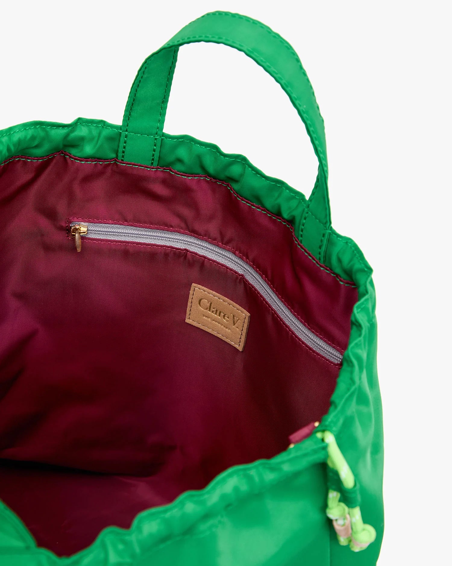 The Sac Tout by Clare Vivier features a green nylon exterior, maroon lining, zippered pocket, leather "Clare V." patch label, and both handles and a crossbody strap for versatile carrying.