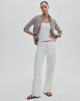 A woman stands against a plain background wearing Rag & Bone's ftwt saige full straight white jeans, a gray checked open shirt over a white tank top, and brown sandals. Her hair is pulled back and one hand rests on her hip.