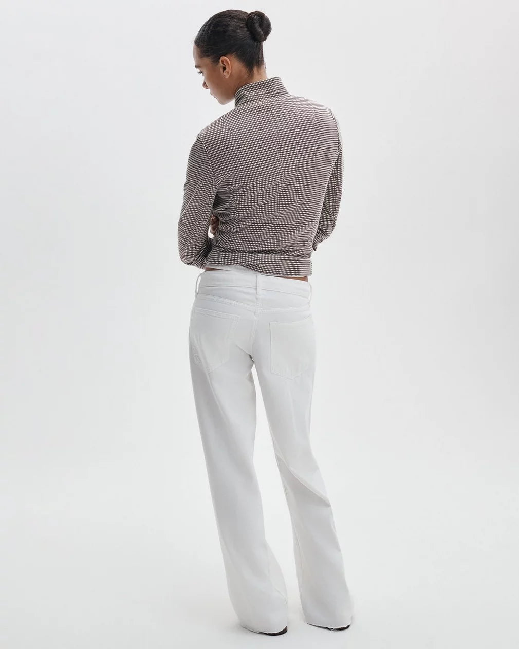 A person stands with their back to the camera, wearing Rag & Bone's ftwt saige full straight jeans and a brown and white striped long-sleeve top, hands on hips, against a plain white background.