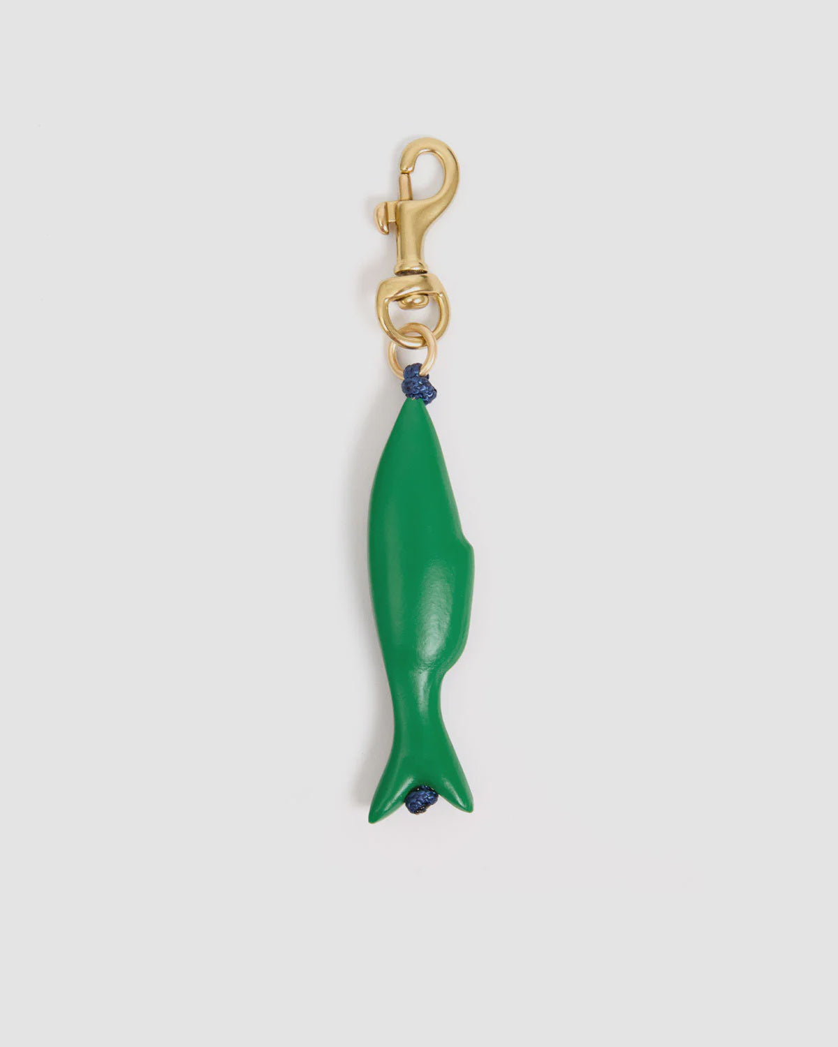 The Sardine FOB by Clare Vivier is a vintage gold-plated brass keychain with a green fish-shaped charm connected by a small blue knot, shown on a plain white background.