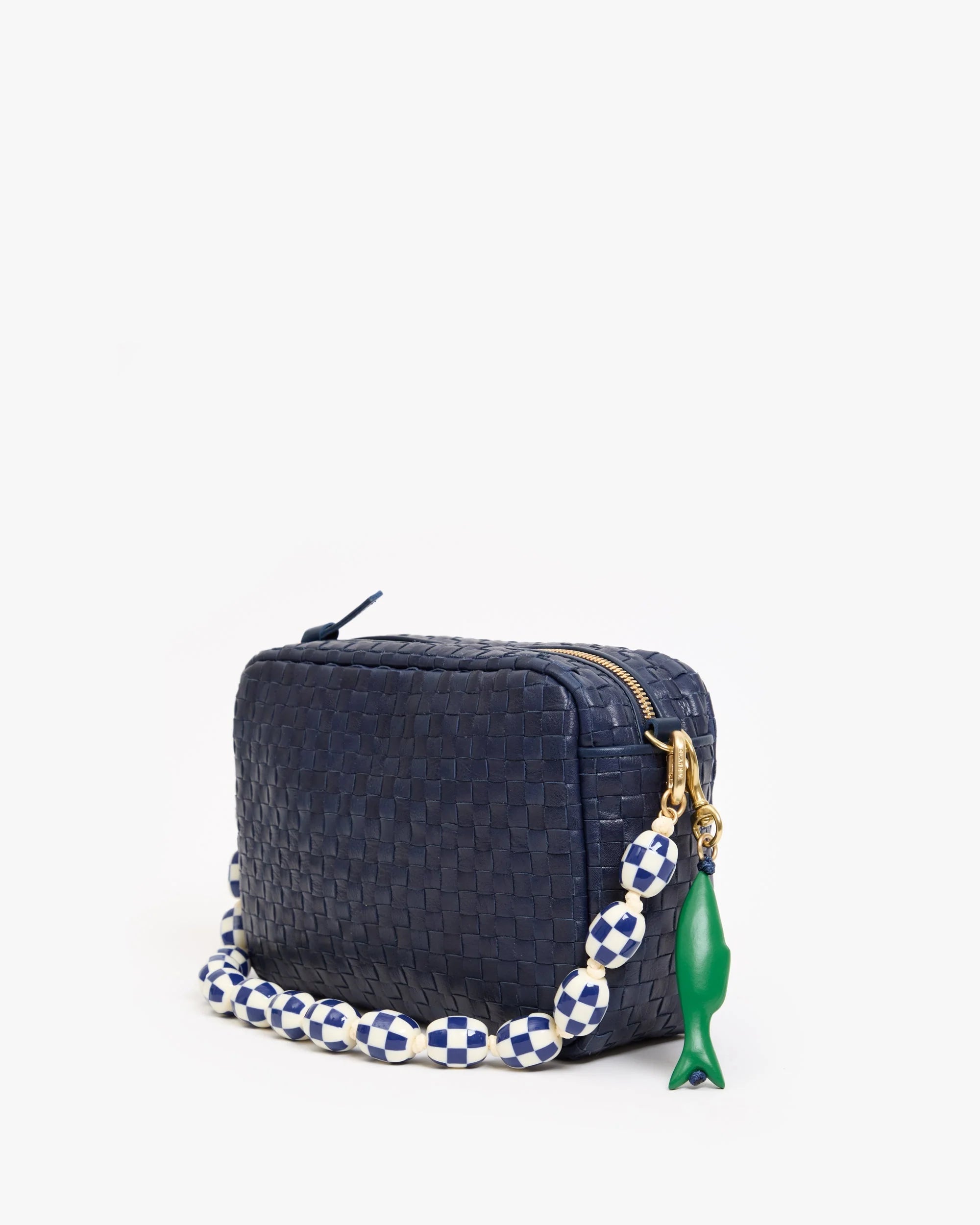 The Clare Vivier Sardine FOB is a small, rectangular navy blue woven handbag featuring a gold zipper, chunky blue-and-white checkered beaded strap, vintage gold-plated brass accents, and a green fish-shaped keychain.