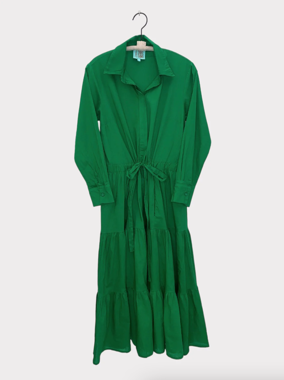 A bright green mid-length dress with long sleeves and a cotton drawstring waist, displayed on a hanger against a plain white background.
