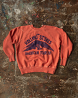 A vintage "The Rolling Stones American Tour '78" Shrunken Sweat in rust orange color, displayed on a textured, multicolored, worn-out background in a Scottsdale Arizona bungalow by Made Worn.