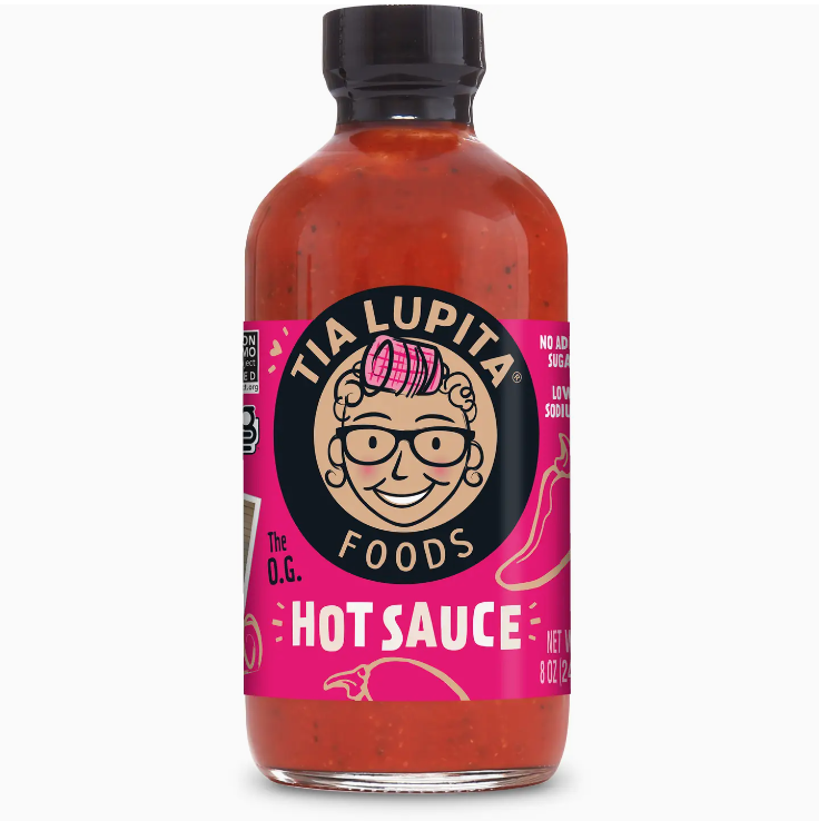 A bottle of Faire Tia Lupita Red Jalapeno Hot Sauce, featuring a pink label with a graphic of a smiling woman wearing glasses and a headscarf, and text describing the sauce as "The O.G. from Scottsdale Arizona.