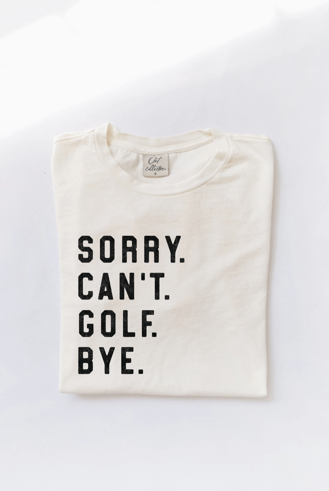 A folded white Oat Collective Sorry Can't Golf Bye Premium Cotton Jersey T-shirt with black text that reads "SORRY CAN'T GOLF BYE" displayed against a white background.