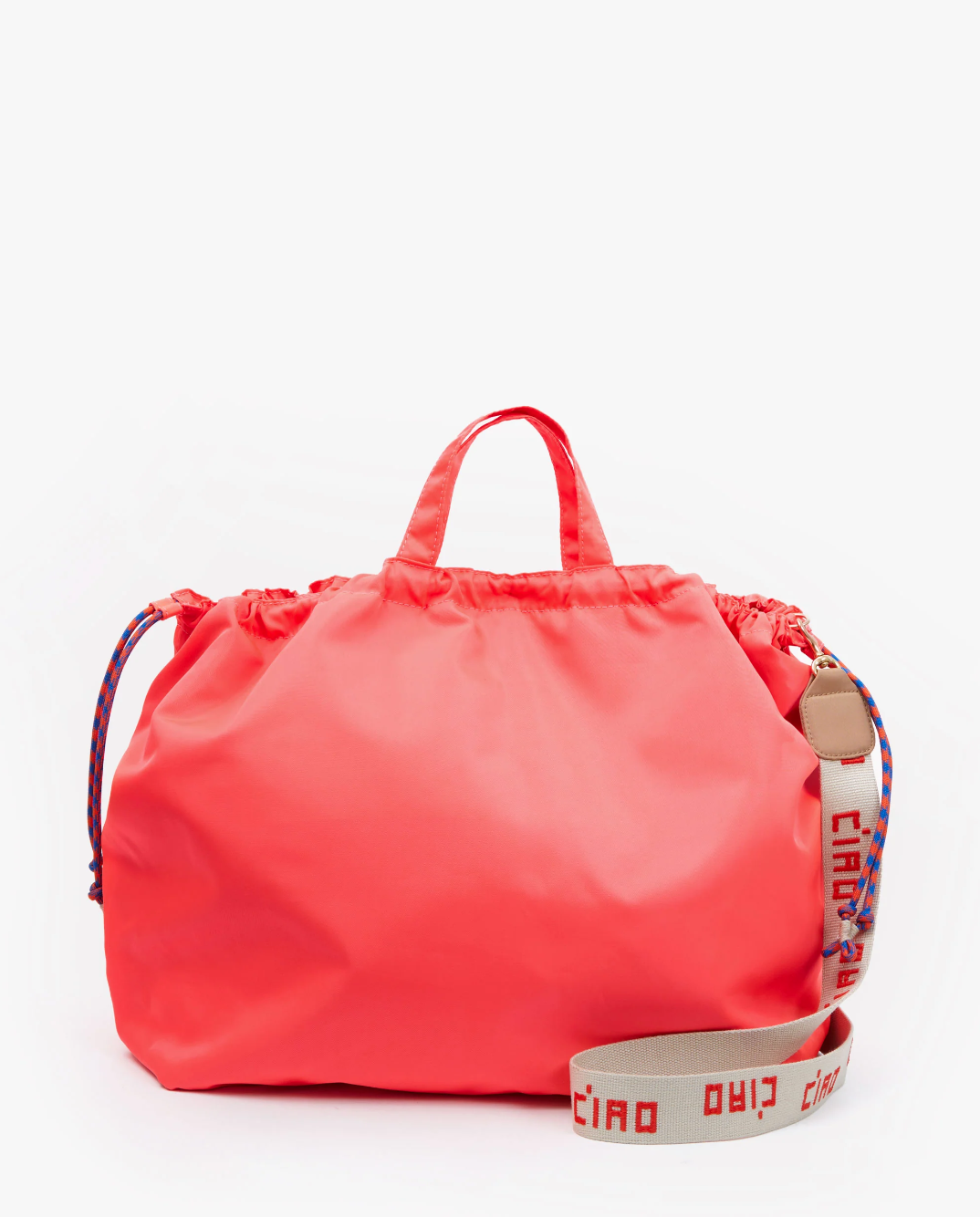 A bright pink drawstring bag with short handles and an adjustable shoulder strap that has "ciao ciao" written on it in red. The strap also features a blue and red design, giving it a lively Arizona style. The background is plain white. This is the Sac Tout from Clare Vivier.