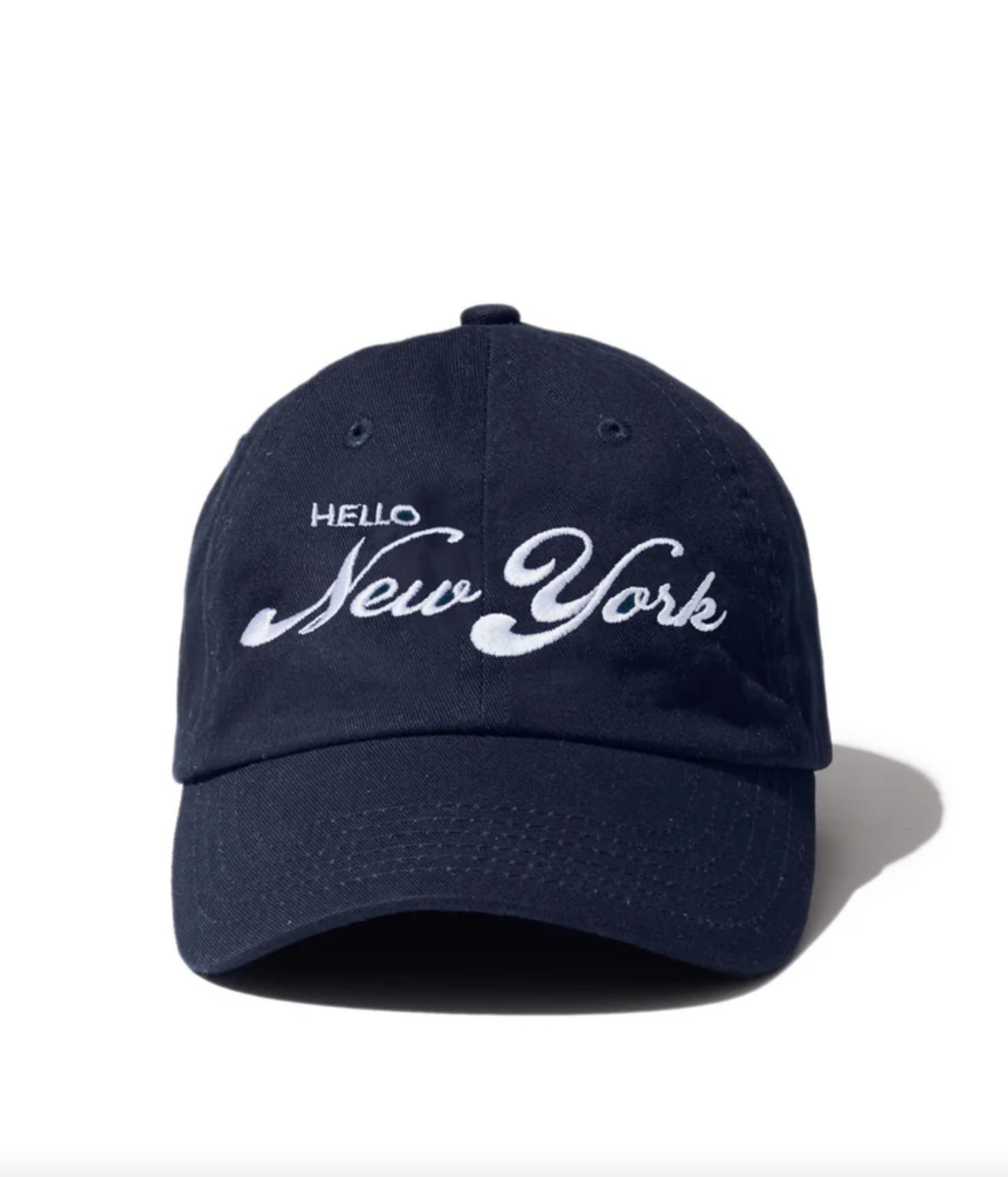 A navy blue cap from Kule's "The New York Kap" collection, featuring the words "Hello New York" embroidered in white on the front. Symbolizing true New Yorker citizenship, the cap is placed against a white background with its shadow visible to the right.