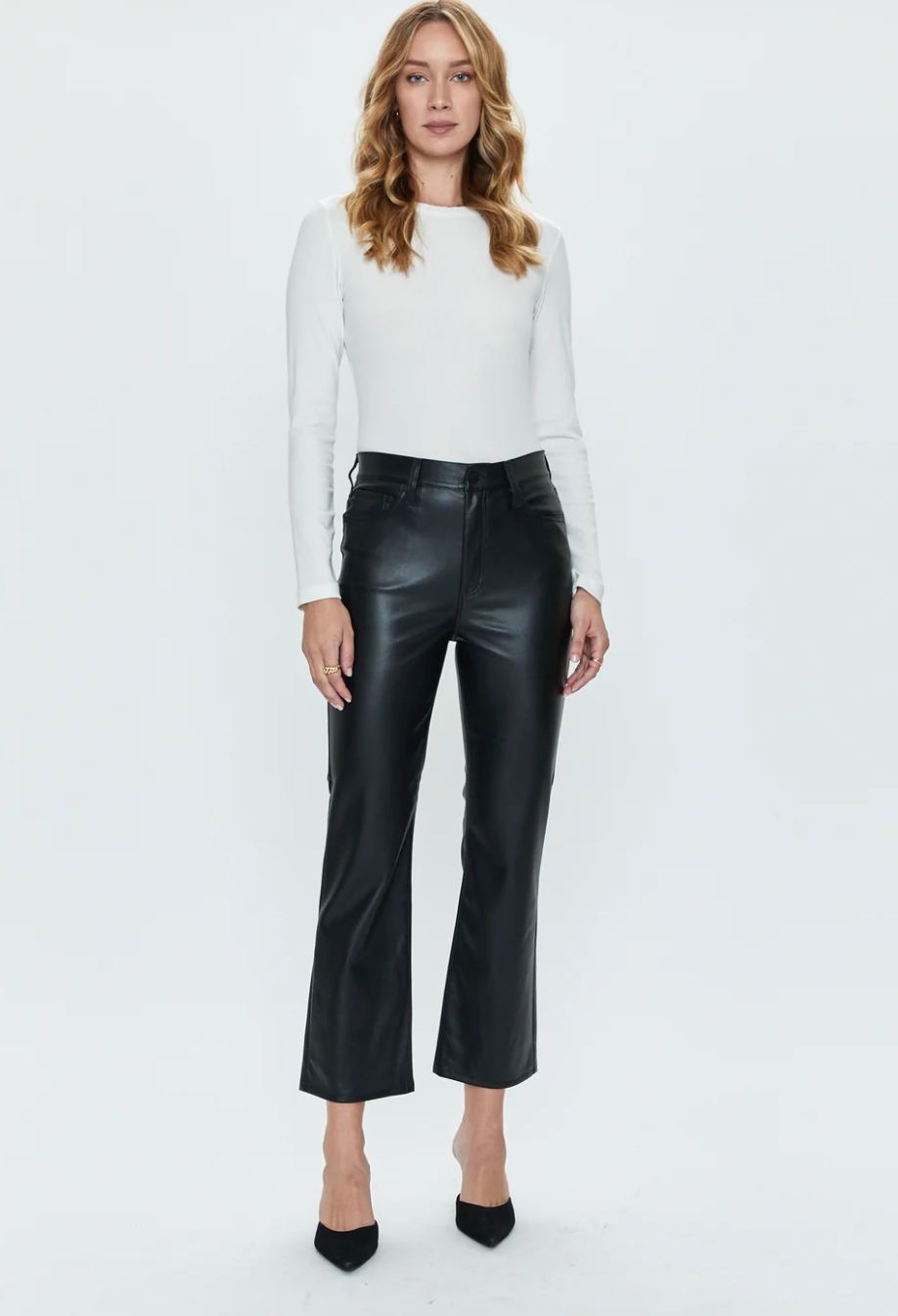 A person with long hair is wearing a fitted white long-sleeve top and the buttery soft black Lennon Pant by Pistola. They are standing against a plain white background and wearing black high-heeled shoes.