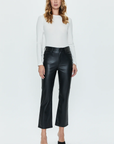 A person with long hair is wearing a fitted white long-sleeve top and the buttery soft black Lennon Pant by Pistola. They are standing against a plain white background and wearing black high-heeled shoes.