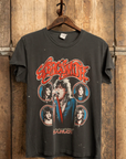 An "Aerosmith In Concert Crew Tee" from Made Worn hangs on a wooden door, featuring an eye-catching graphic bursting with vibrant illustrations of the band members and "IN CONCERT" in bold red. Handmade in Los Angeles, this unisex tee has a vintage cotton construction that exudes a charmingly worn, retro style.