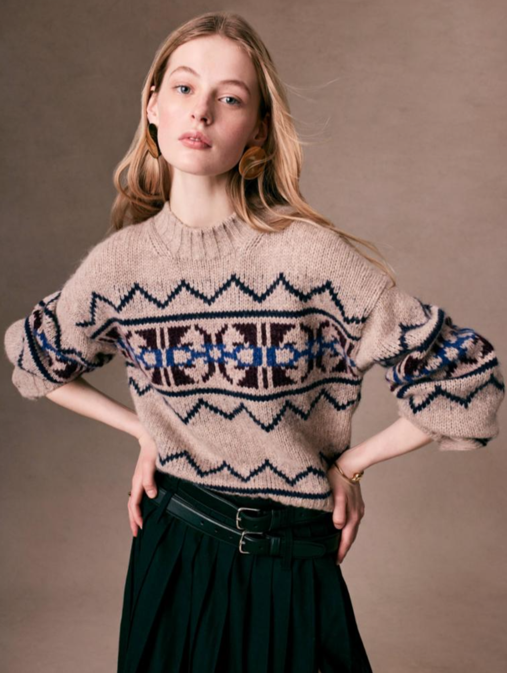 A person stands confidently against a neutral background, wearing the Plush Alpaca Blend Fair Isle Crewneck from White + Warren, featuring a cozy geometric blue and brown pattern. Their long, light hair complements the relaxed pose, with one hand resting on their hip. They also wear a black skirt with belts, embodying cozy winter fashion.