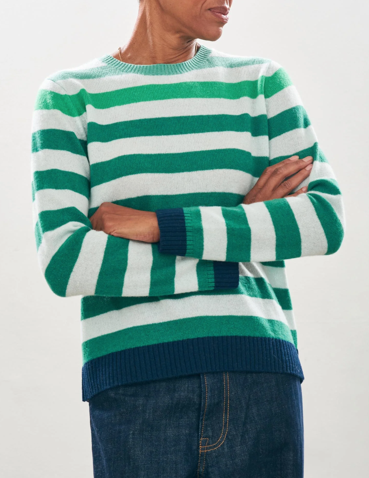 A person in the Gradient Stripe Crew Multi by Jumper 1 2 3 4/CR2 is crossing their arms. They are also wearing dark blue pants, standing against a plain light gray background.