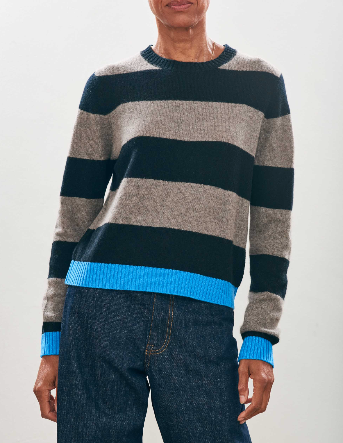 Wearing the Contrast Stripe Crew sweater from Jumper 1 2 3 4/CR2, with gray and black stripes and blue cuffs and hem, paired with blue jeans, this look perfectly embodies the signature style of Jumper 1234.