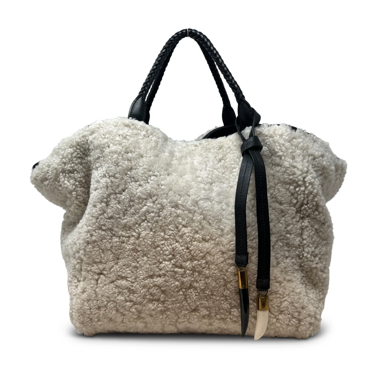 The Square Tote Natural Shearling with two handles by Kempton & Co. is a luxurious bag crafted from soft, cream-colored shearling. This large, fluffy tote features black braided leather handles and elegant tassel details with gold accents, offering a perfect blend of comfort and style in its relaxed, cozy appearance.