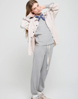 Against a light background, a person models in a beige jacket and the Venice Sweats from ATF Clothing. Beige sneakers complement the look, while a navy blue bandana adds flair as they adjust their hairstyle.