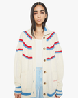 A woman with long dark hair models The Mock Neck Button Cardigan by Mother, featuring a slouchy fit with blue and red stripes over a white top. This alpaca cotton blend cardigan has large buttons and two front pockets, set against a plain white background.