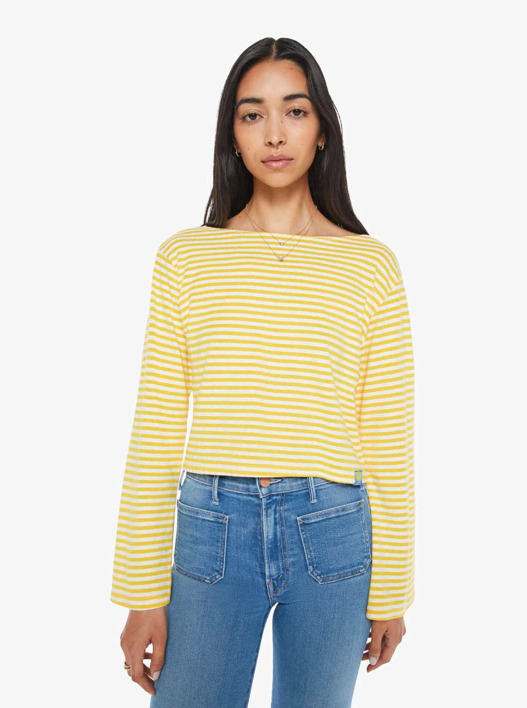 A person with long dark hair wears The Skipper Bell LS Tee from Mother, featuring yellow and white horizontal stripes, paired with blue jeans. They stand against a plain white background, looking forward with a neutral expression.