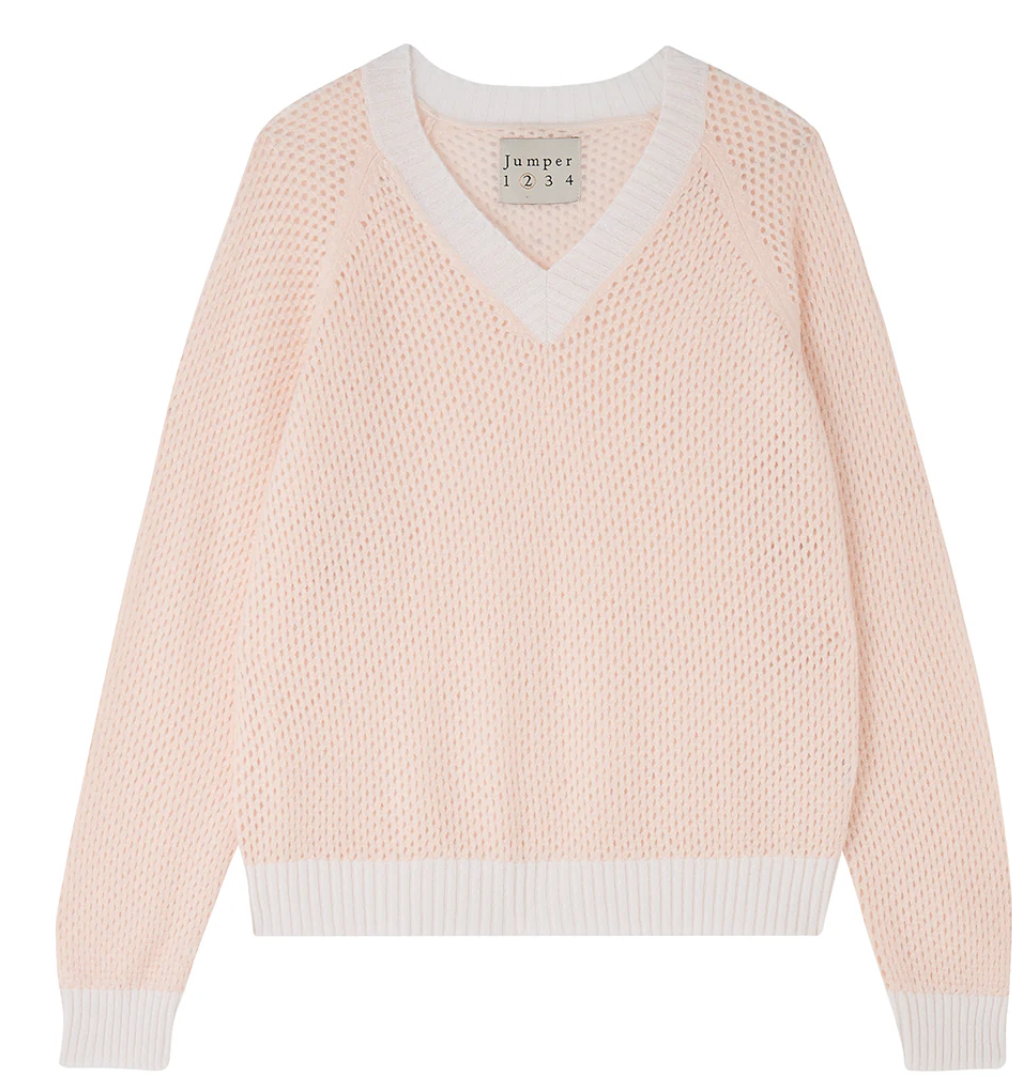 The Holey Contrast Vee from Jumper 1 2 3 4/CR2 is a light pink cashmere jumper featuring an airy, textured knit with white trim on the V-neckline, cuffs, and hem. It offers an oversized fit.