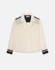 The FRAME Silk Pajama Shirt is a cream blouse with long sleeves, a button-up front, and black accents on cuffs, shoulders, and a stripe on the upper sleeve. Made from 100% silk, it features a notched collar and an elegant silhouette for a loose fit.